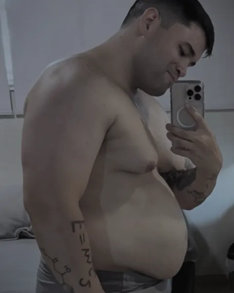Miguel de perfil frente al espejo, en su punto más pesado, con el tatuaje E=mc² en el antebrazo.